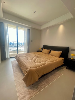 Une chambre moderne avec un grand lit, une table de chevet et une vue sur le paysage urbain, grâce à de grandes fenêtres.