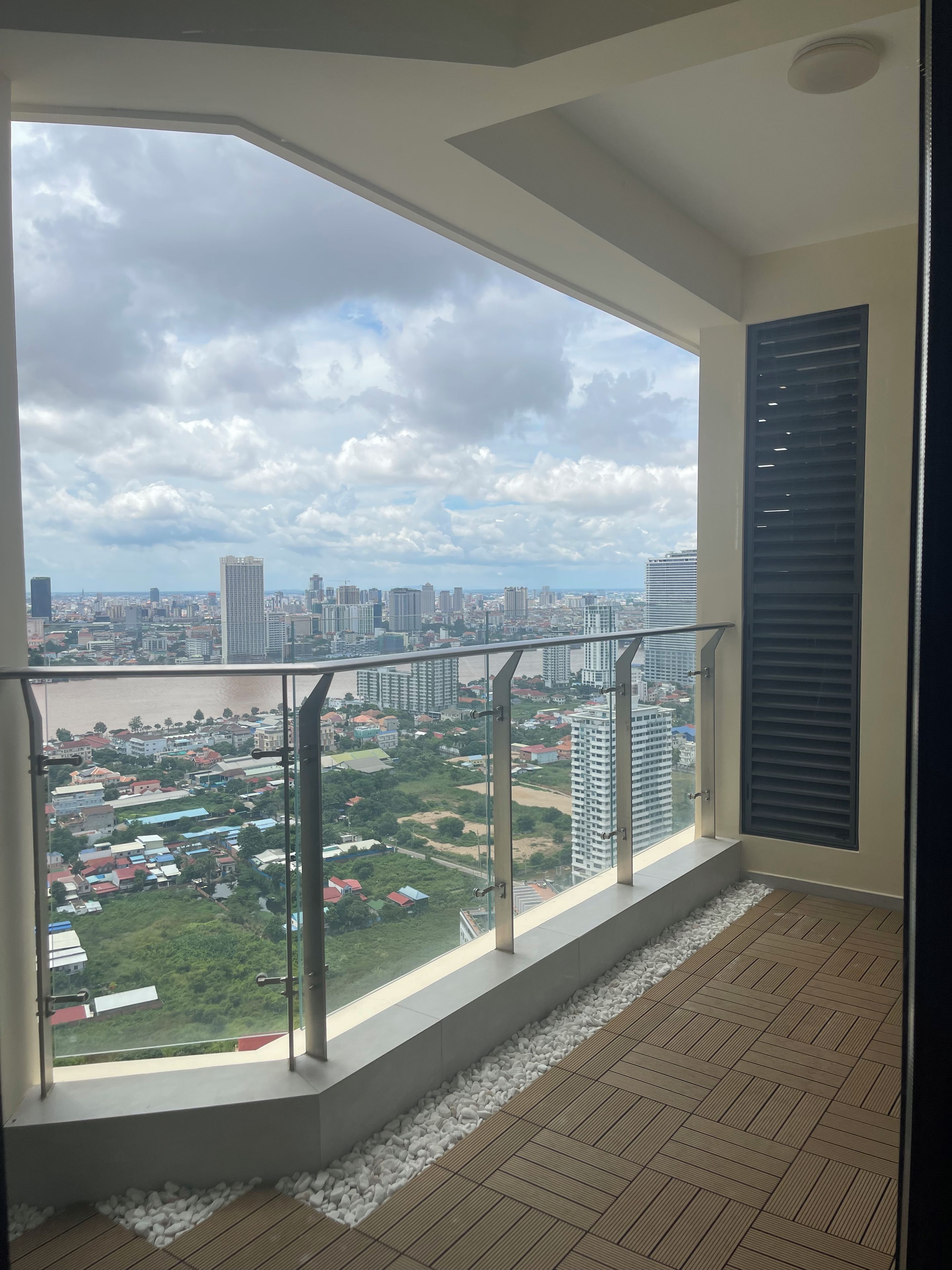 Ein Zimmer mit großem Fenster und Blick auf eine Stadtlandschaft, inklusive Balkon mit Metallgeländer und Fliesenboden.