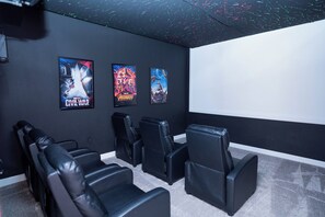 A home theater with black leather recliners, a large screen, and movie posters on the wall. - 6BR Pool Home w/ Theater & Game Room (Davenport)