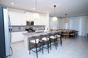Una cucina moderna con mobili bianchi, elettrodomestici in acciaio inossidabile e un'isola centrale con sgabelli da bar.