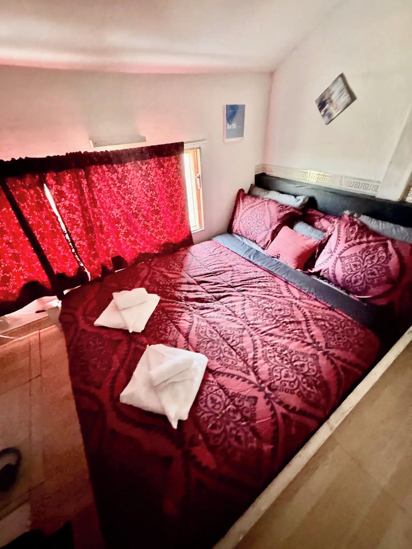 A bedroom with a large bed, a headboard, and a window with red curtains.