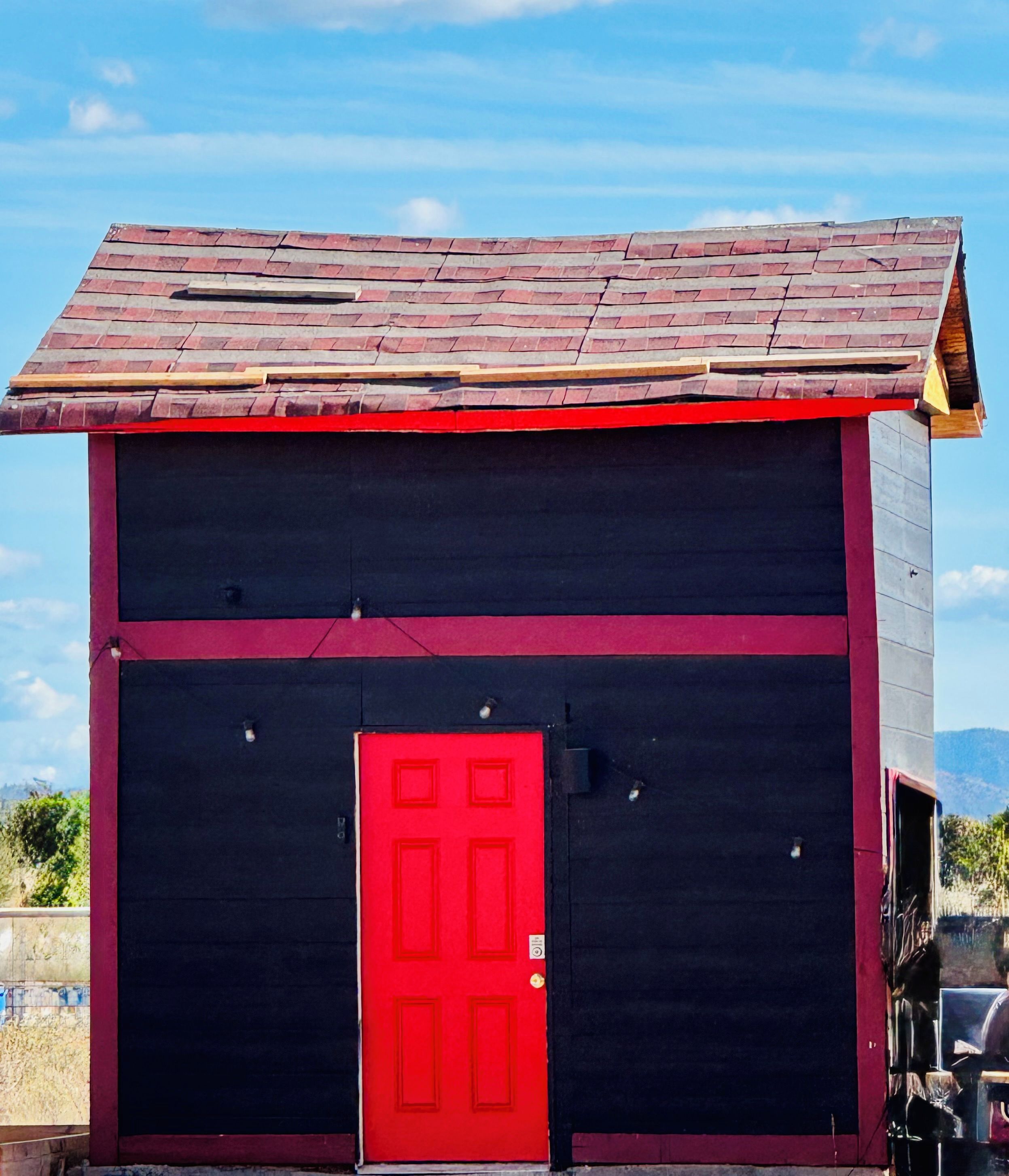 A small, two-story building with a red door and a sloped roof.
