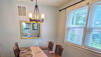 A dining room with a wooden table, chairs, a chandelier, and a window with blinds.