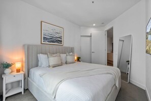 A bedroom with a bed, bedside lamps, a nightstand, a large mirror, and a framed picture on the wall. - The Southbank King - Pool, Gym and Tram, near CBD (Southbank)