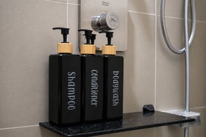 Drei schwarze Flaschen mit Holzbeschlägen auf einer schwarzen Arbeitsplatte in einem Badezimmer.