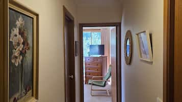 Un pasillo con una lámpara en el techo, un cuadro enmarcado, un aparador de madera y una silla verde.