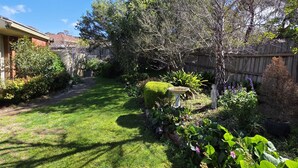 Un jardin bien entretenu avec une pelouse, divers arbustes, une clôture en bois et un arbre.