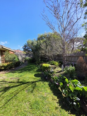 A well-maintained backyard with a lawn, various shrubs, a wooden fence, and a tree. - 🌿 Private Queen Bedroom, Private Bathroom & Garden Retreat in Sunbury (Sunbury)