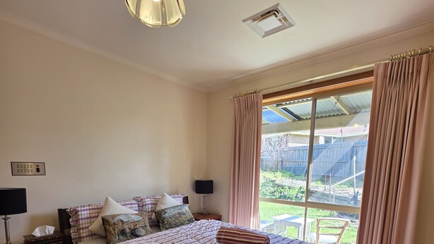 Une chambre avec un grand lit, une table de chevet avec une lampe, une fenêtre avec des rideaux et une vue sur l’extérieur.
