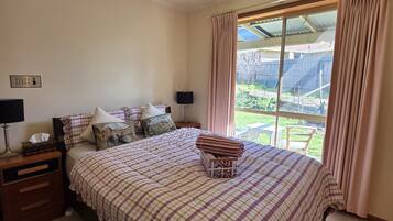 A bedroom with a large bed, a bedside table with a lamp, a window with curtains, and a view of the outdoors.
