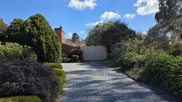 A paved pathway leading through a landscaped garden with various shrubs and trees.