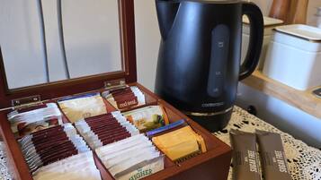 A tea box with compartments containing various tea bags, a black coffee maker, and a sugar-free tea packet on a table with a lace doily.
