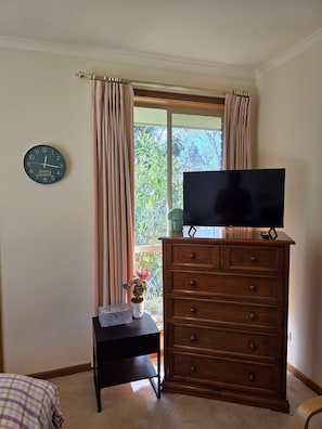 Una habitació amb un taulell de fusta, un televisor a sobre, un rellotge a la paret i una finestra amb cortines.