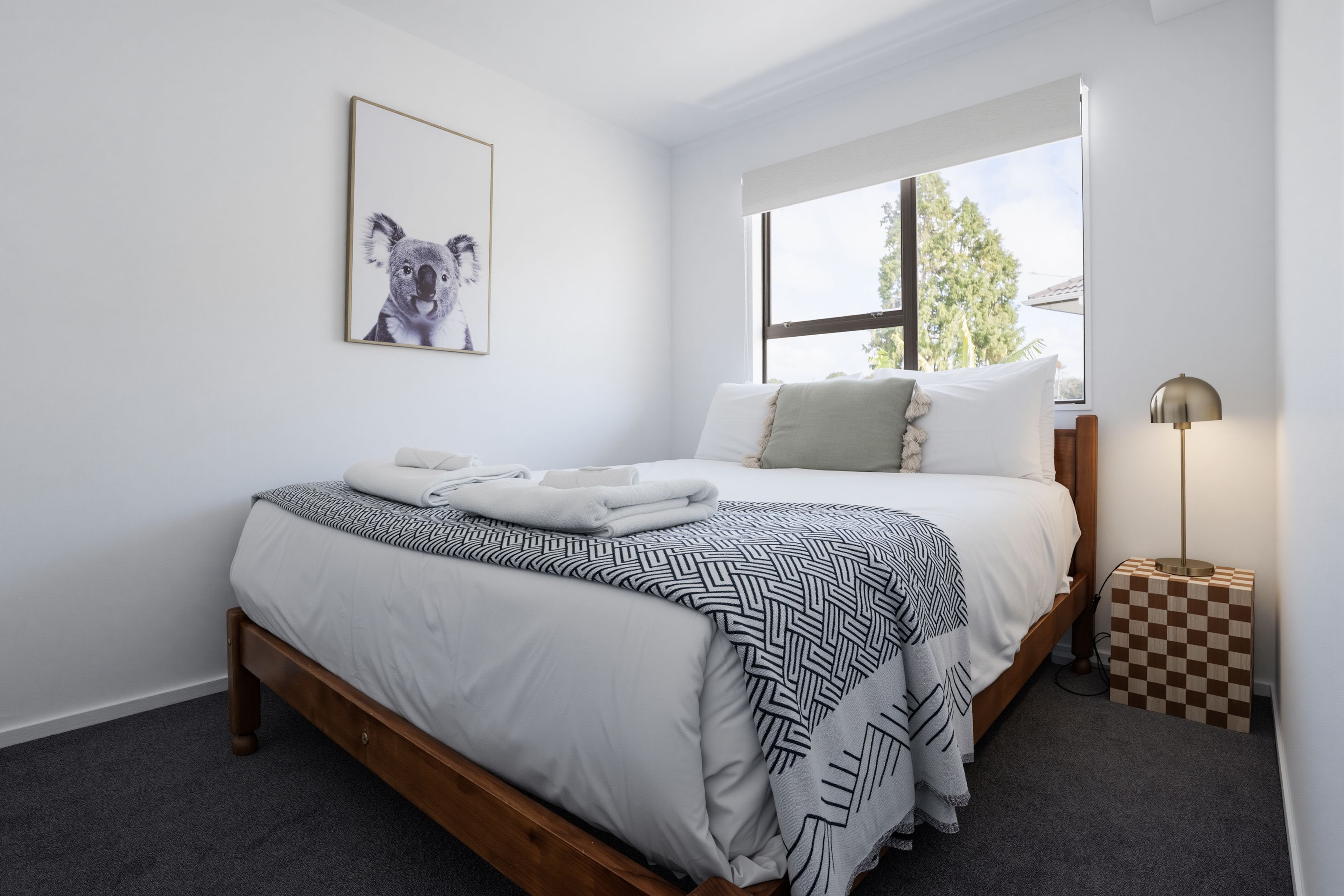 A bedroom with a bed, a framed picture on the wall, a window, and a floor lamp.