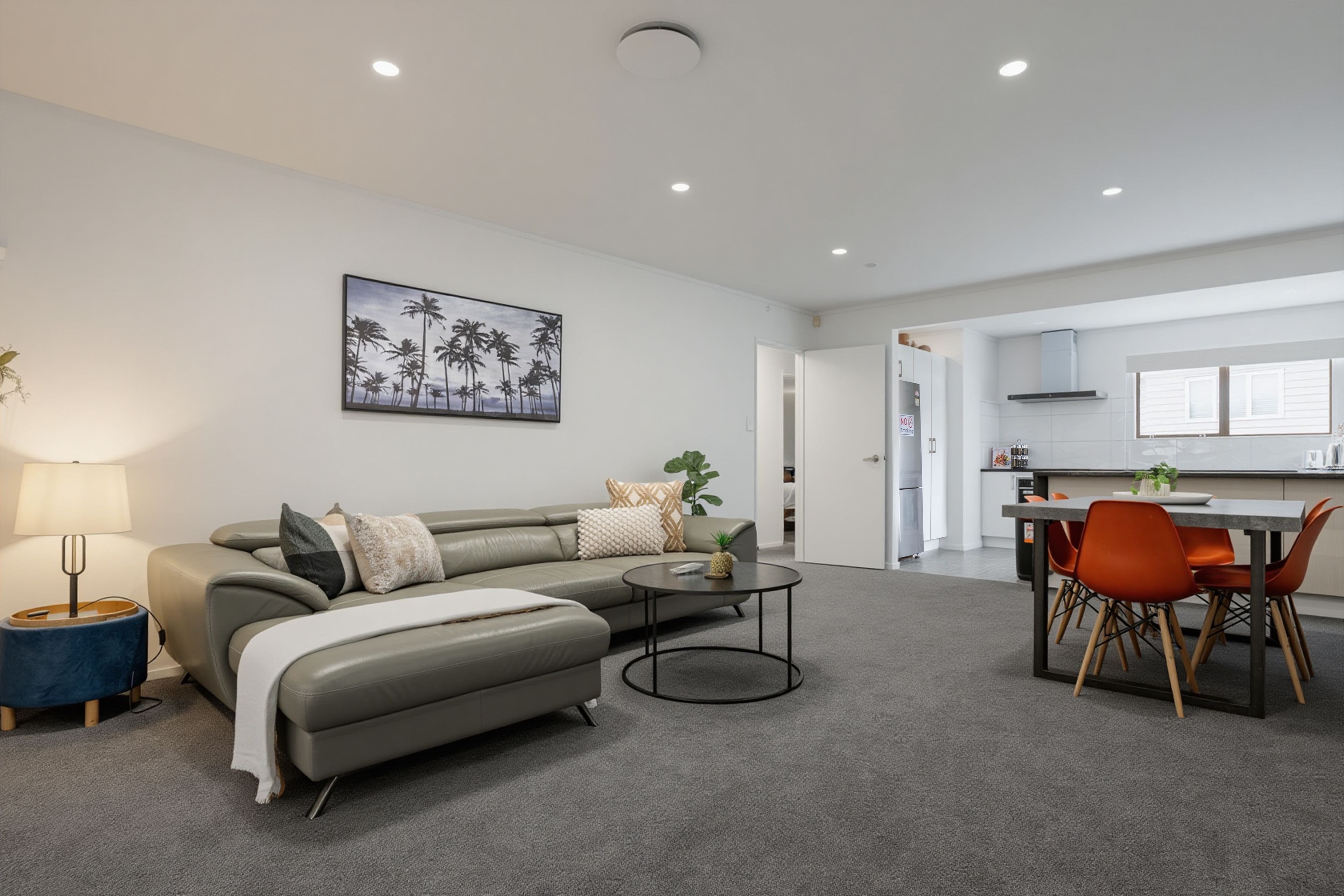A modern living room with a sofa, coffee table, and a painting of palm trees.
