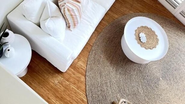 Um sofá branco com almofadas listradas, uma mesa de centro redonda e uma planta grande.