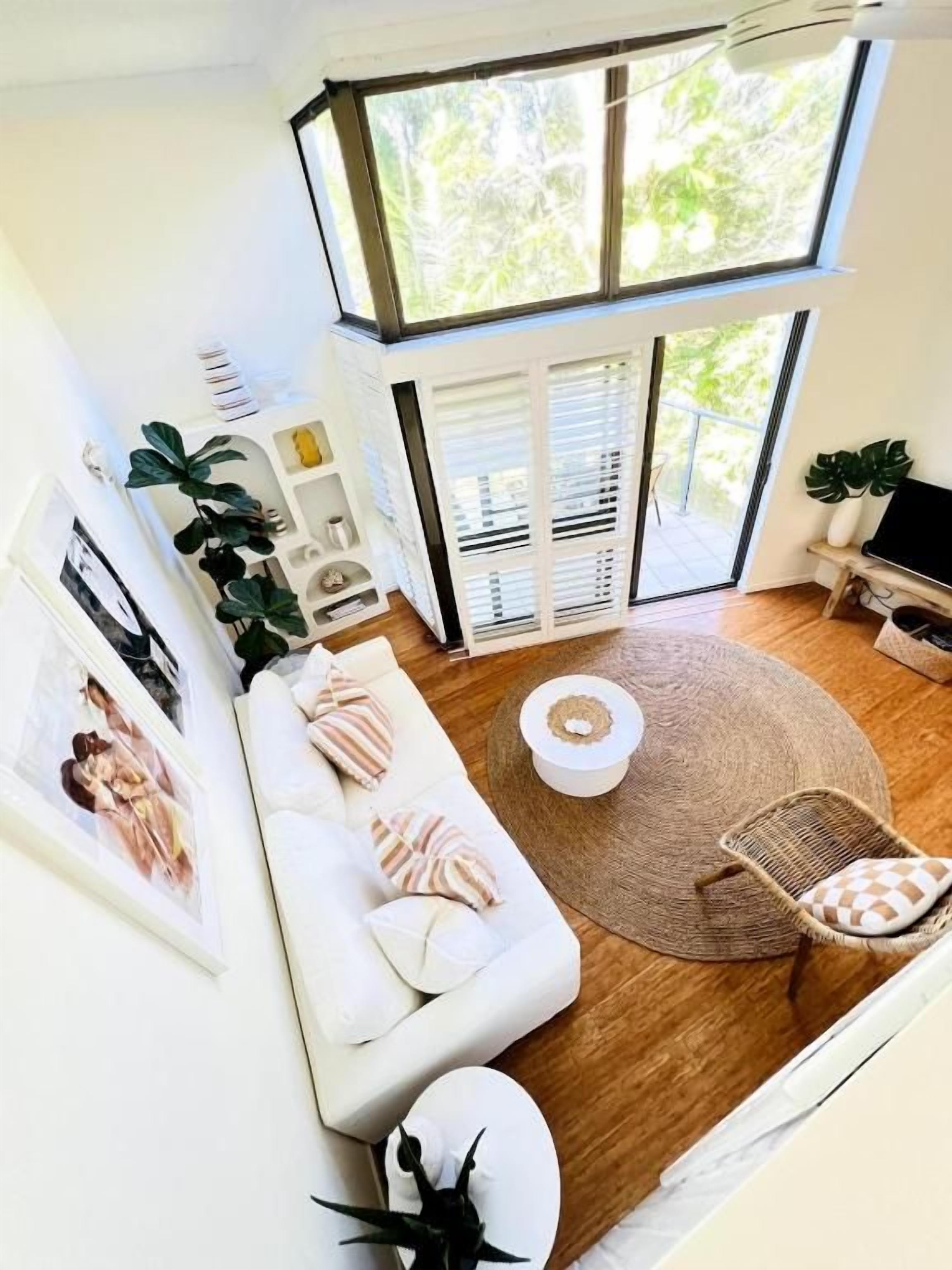 A modern living room with a white sofa, a round coffee table, and a large window overlooking greenery.