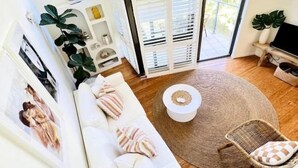 Uma sala de estar moderna com um sofá branco, uma mesa de centro redonda e uma janela grande com vista para o verde.