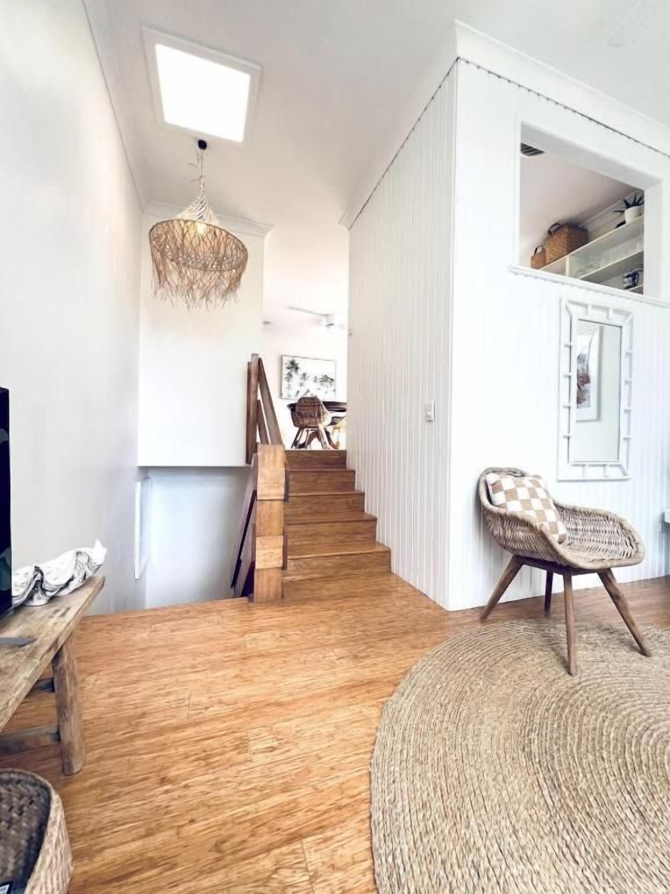 A staircase leading to a second floor, a wicker chair, and a woven rug in a room with wooden flooring and white walls.