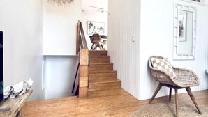 Escada que leva a um segundo andar, uma cadeira de vime e um tapete tecido em um quarto com piso de madeira e paredes brancas.