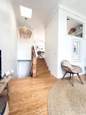 A staircase leading to a second floor, a wicker chair, and a woven rug in a room with wooden flooring and white walls. - Suntan @ Sunshine - seconds from shops & beach (Sunshine Beach)