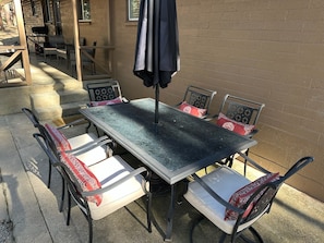 En uteplats med ett metallbord och stolar, en grill och en mur av tegelsten.