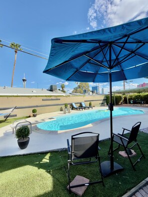 Zona de piscina amb gandules, un gran parasol i vista a una torre al fons.