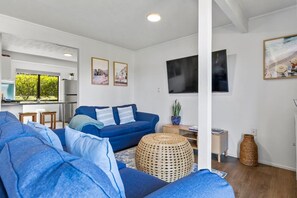 A modern living room with a blue sofa, a woven ottoman, and a flat-screen TV mounted on the wall. - Marina Views Apartment 2 - downstairs apartment (Taupō)