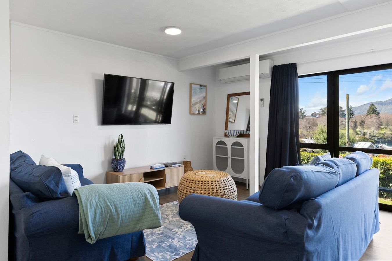 A modern living room with two sofas, a flat-screen TV, a small cabinet, and a large window with a view.