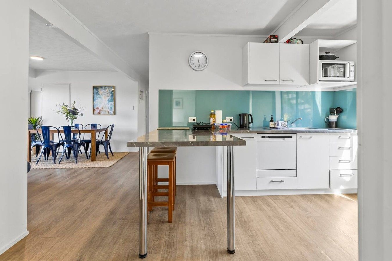 A modern kitchen with a central island, white cabinetry, and a teal backsplash.