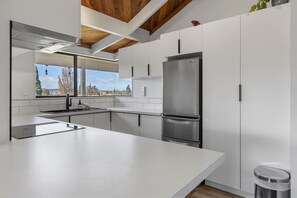 Eine moderne Küche mit einem Edelstahl-Kühlschrank, weißen Schränken und einem großen Fenster mit Blick ins Freie.