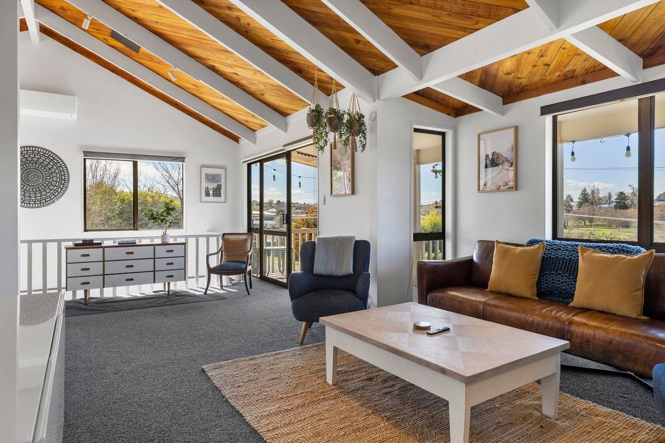 A spacious living area with a wooden ceiling, a sofa, a coffee table, and a view through large windows.