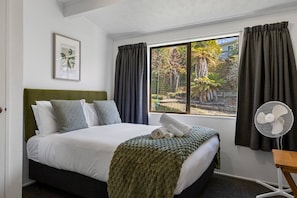 Ein Hotelzimmer mit Bett, einem Vorhangfenster, einem Ventilator und einem gerahmten Bild an der Wand.