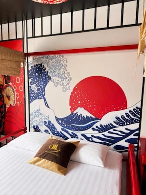 Uma cama com travesseiro, parede com pintura de ondas japonesas e cabeceira vermelha.