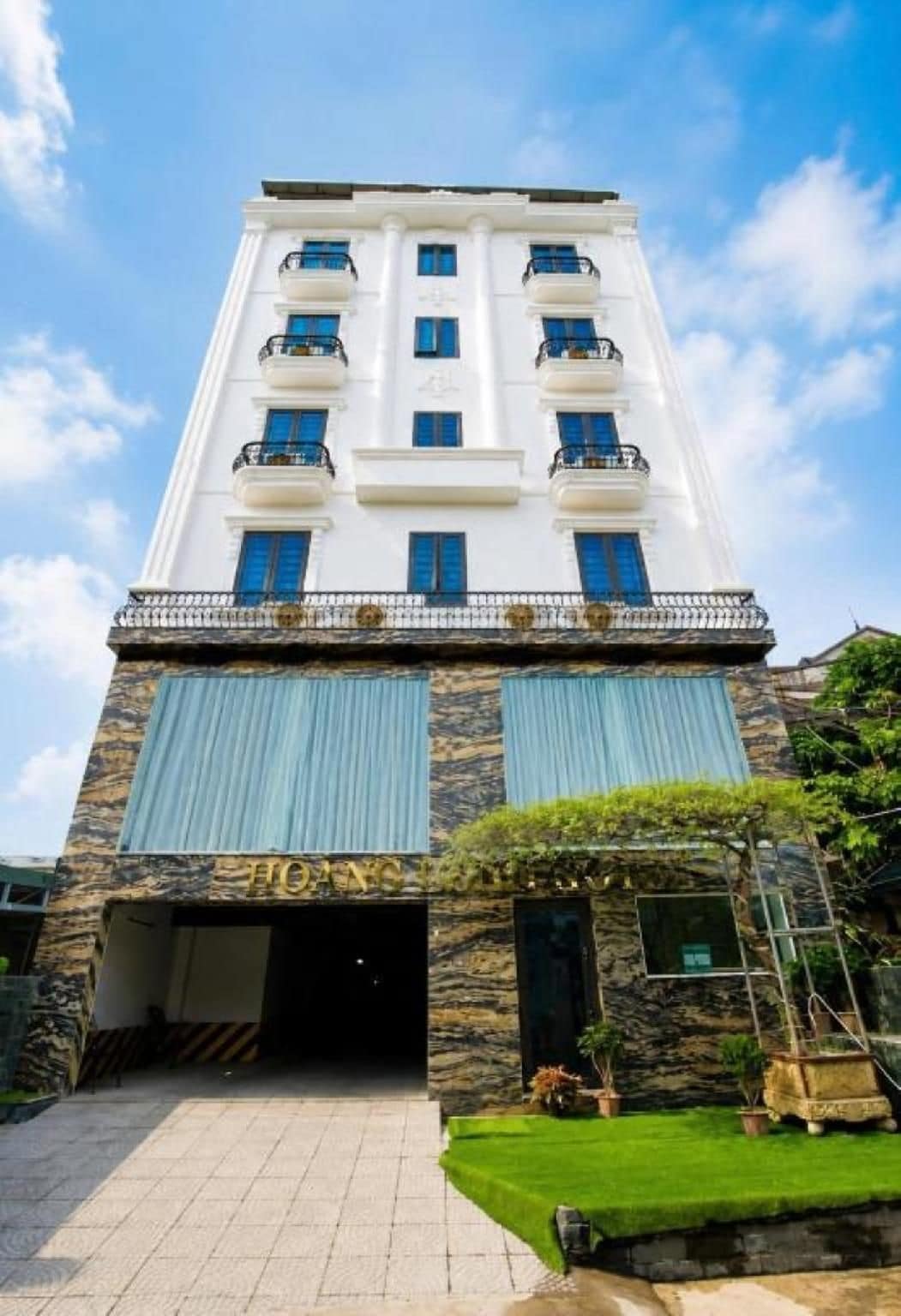 A multi-story hotel with a central entrance, a stone facade, and a clear sky.