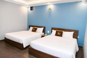 Duas camas de solteiro com cabeceiras de madeira e roupa de cama branca, em quarto com paredes azuis e chão de azulejos.