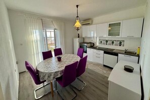 A compact kitchen with white cabinets, a dining table with purple chairs, and a hanging light fixture. - Three bedroom apartment with terrace and sea view Podstrana, Split (A-27996-a) (Podstrana)