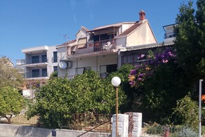 A multi-story residential building with balconies, a satellite dish, and a garden with purple flowers. - Three bedroom apartment with terrace and sea view Podstrana, Split (A-27996-a) (Podstrana)