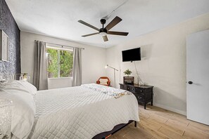 A bedroom with a bed, a ceiling fan, a TV, a dresser, and a window with curtains. - Paradise Pkwy Getaway in Phoenix + Pool (Phoenix)