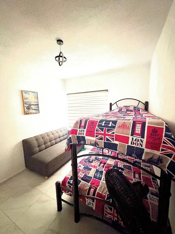 A bedroom with a bed covered in a quilt, a bench, a painting on the wall, and a window with blinds. - Acapulco shines! Beautiful apartment. Just 15 minutes from Puerto Márquez and P. Diamante (Acapulco de Juárez)