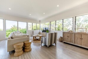 A modern living room with a sofa, coffee table, and striped armchair. There is a wooden cabinet and a television on a stand. - Luxe Sunshine Beach House - 30m to Beach! (Sunshine Beach)