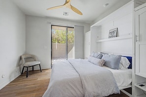 Ein Schlafzimmer mit einem Bett, einem Sessel, einem Deckenventilator und einer Tür, die auf einen Balkon führt.