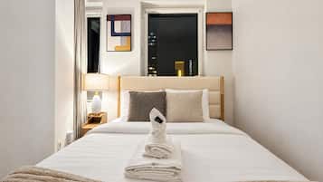 A hotel room with a bed, a nightstand, a lamp, and a window with a city view.
