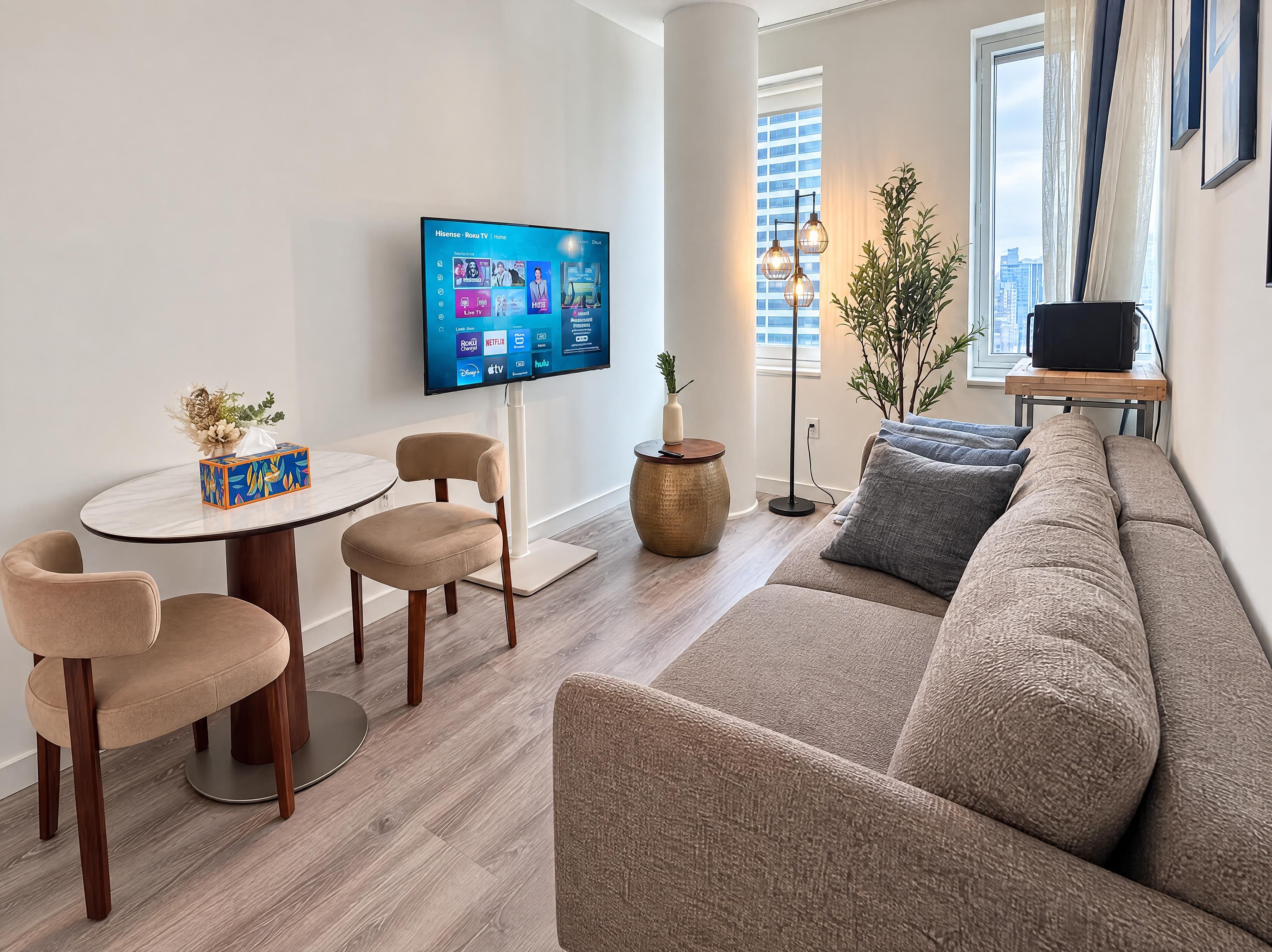 Ein modernes Wohnzimmer mit Flachbildfernseher, einem runden Esstisch, zwei Stühlen, einer Couch und einer Stehlampe.