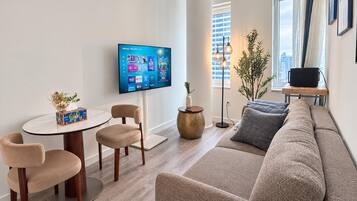 Ein modernes Wohnzimmer mit Flachbildfernseher, einem runden Esstisch, zwei Stühlen, einer Couch und einer Stehlampe.