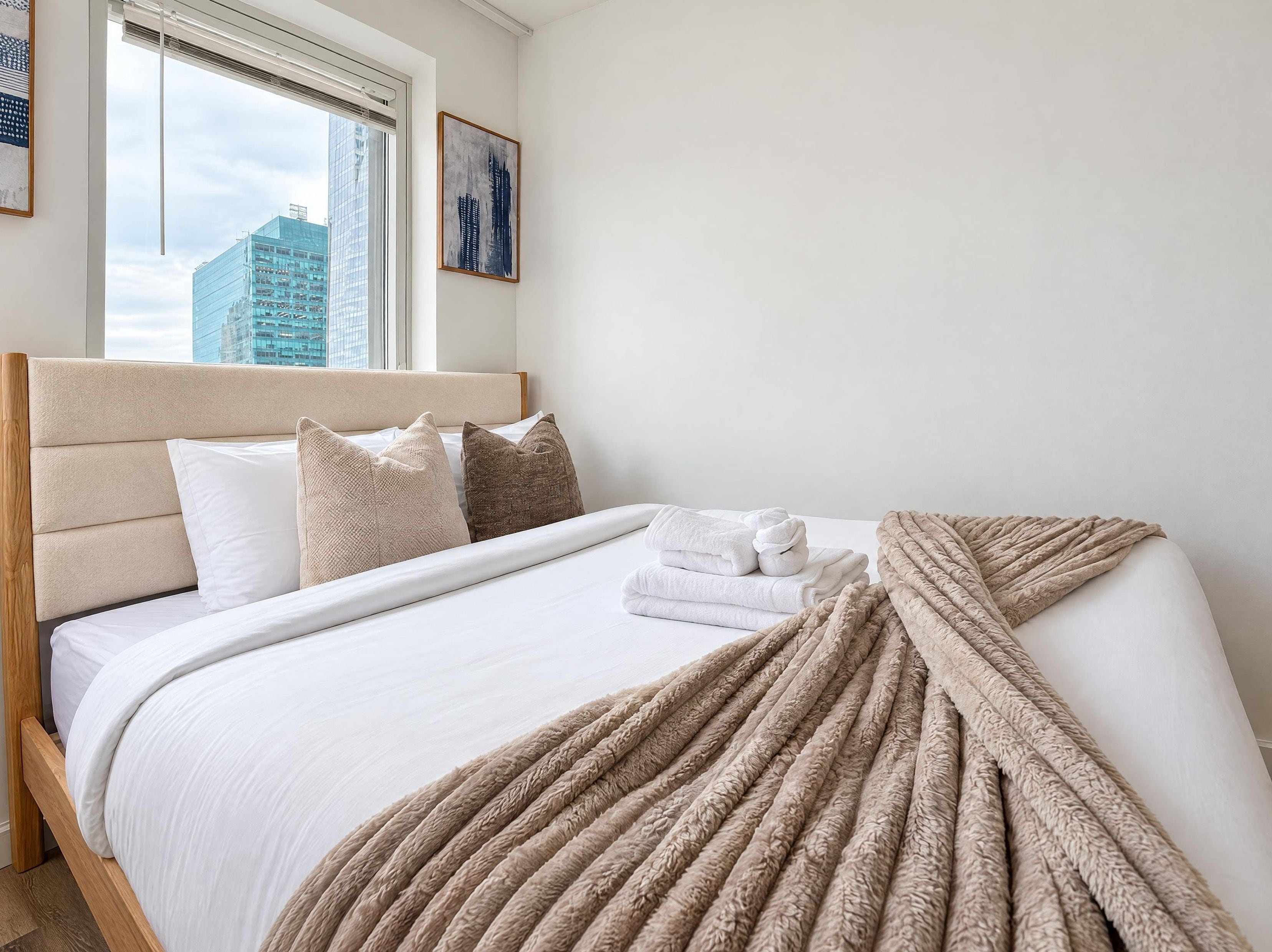 Habitación de hotel con una cama, almohadas, una colcha y vistas a la ciudad a través de la ventana.