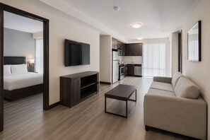 A modern hotel room with a bed, a TV, a dark wooden entertainment unit, a small table, a sofa, and a kitchenette. - Modern Manhattan Condo Near Times Square (New York)
