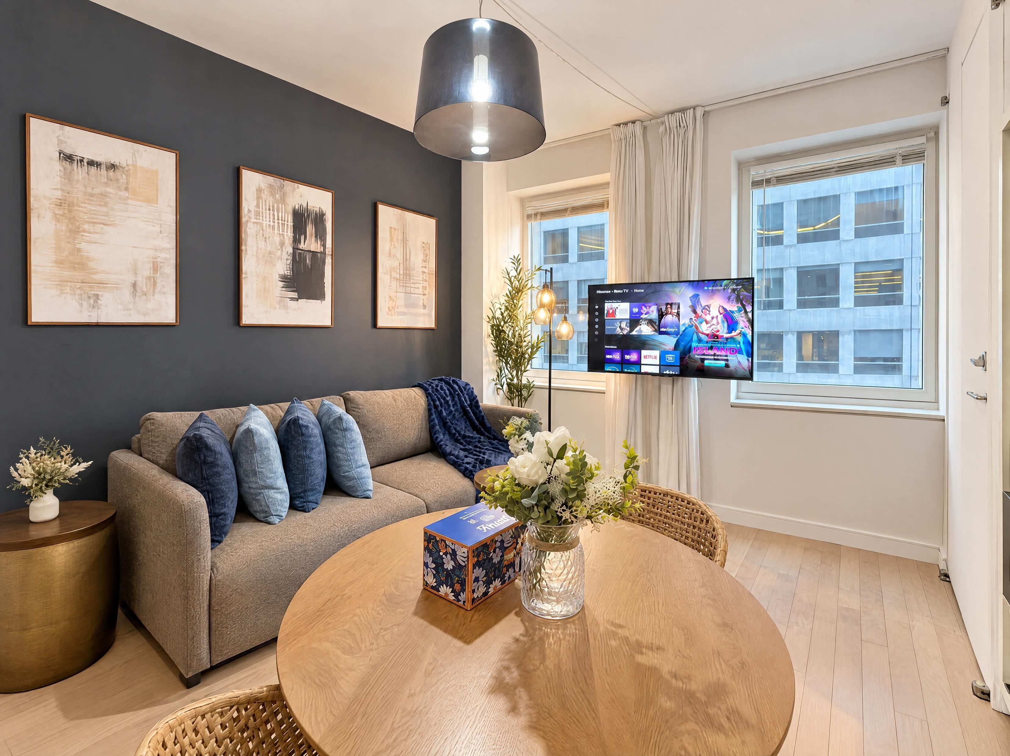 A modern living room with a sofa, a round wooden table, and a TV mounted on the wall.