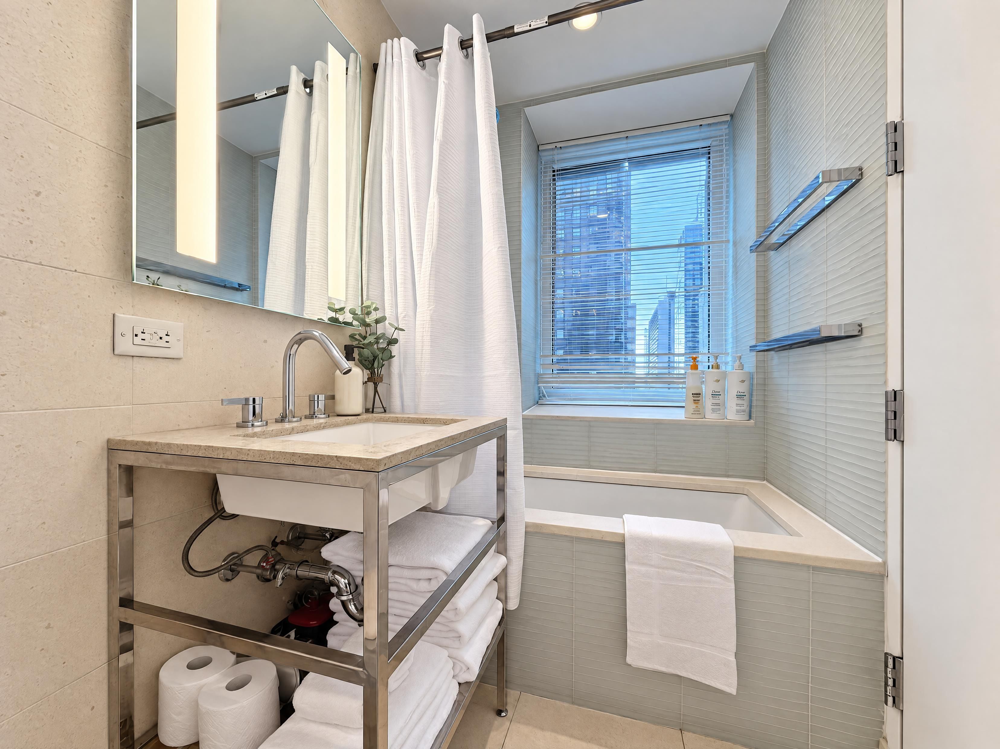 Un baño moderno con tocador, bañera, ventana con persianas y un perchero para toallas.
