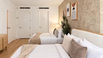 Een hotelkamer met twee bedden, een houten vloer, een wand met abstracte kunst en een plant.
